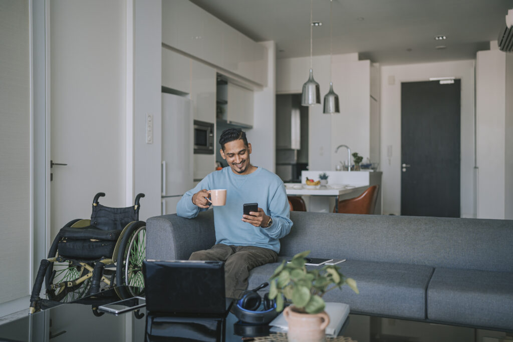 Man relaxing on the sofa with a smartphone and a mug, a wheelchair nearby