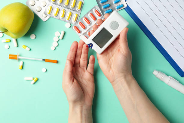 Using a glucose meter to check blood sugar for diabetes management surrounded by pills and an apple