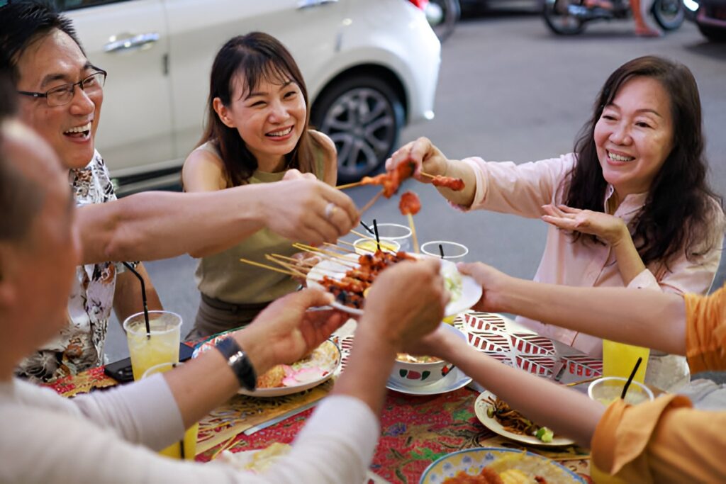 Colleagues sharing satay at an outdoor hawker table, a common meal setting for prediabetic office workers